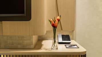 A modern hotel reception desk with a flat-screen TV, a vase with orange flowers, a telephone, and a small table.