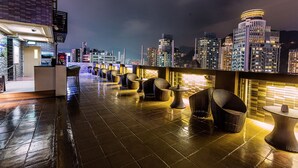 A rooftop terrace with wicker furniture and a city skyline view. - Burlington Hotel (Hong Kong)