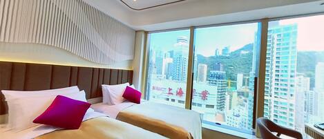 Une chambre d’hôtel avec un grand lit, deux oreillers, une chaise et une vue sur le paysage urbain, visible à travers de grandes fenêtres.