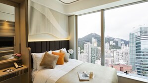 A modern hotel room with a large bed, a bedside table with a lamp, a mirror, and a view of the cityscape. - Burlington Hotel (Hong Kong)