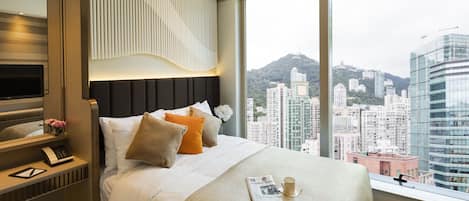 A modern hotel room with a large bed, a bedside table with a lamp, a mirror, and a view of the cityscape.