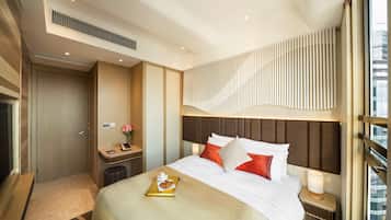 A modern hotel room with a large bed, a bedside table with a lamp, a small desk with a chair, and a large window offering a city view.