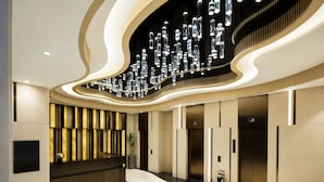 A modern lobby with a curved reception desk, elevators, and a decorative light fixture. - Burlington Hotel (Hong Kong)