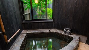 A stone hot tub with a wooden bench, a window with a view of greenery, and a small heater. - Yurari Rokumyo (Yufu)