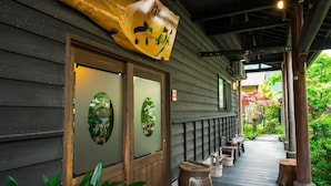 A traditional Japanese building with a wooden exterior, a large wooden sculpture above the entrance, and a pathway leading to a garden. - Yurari Rokumyo (Yufu)