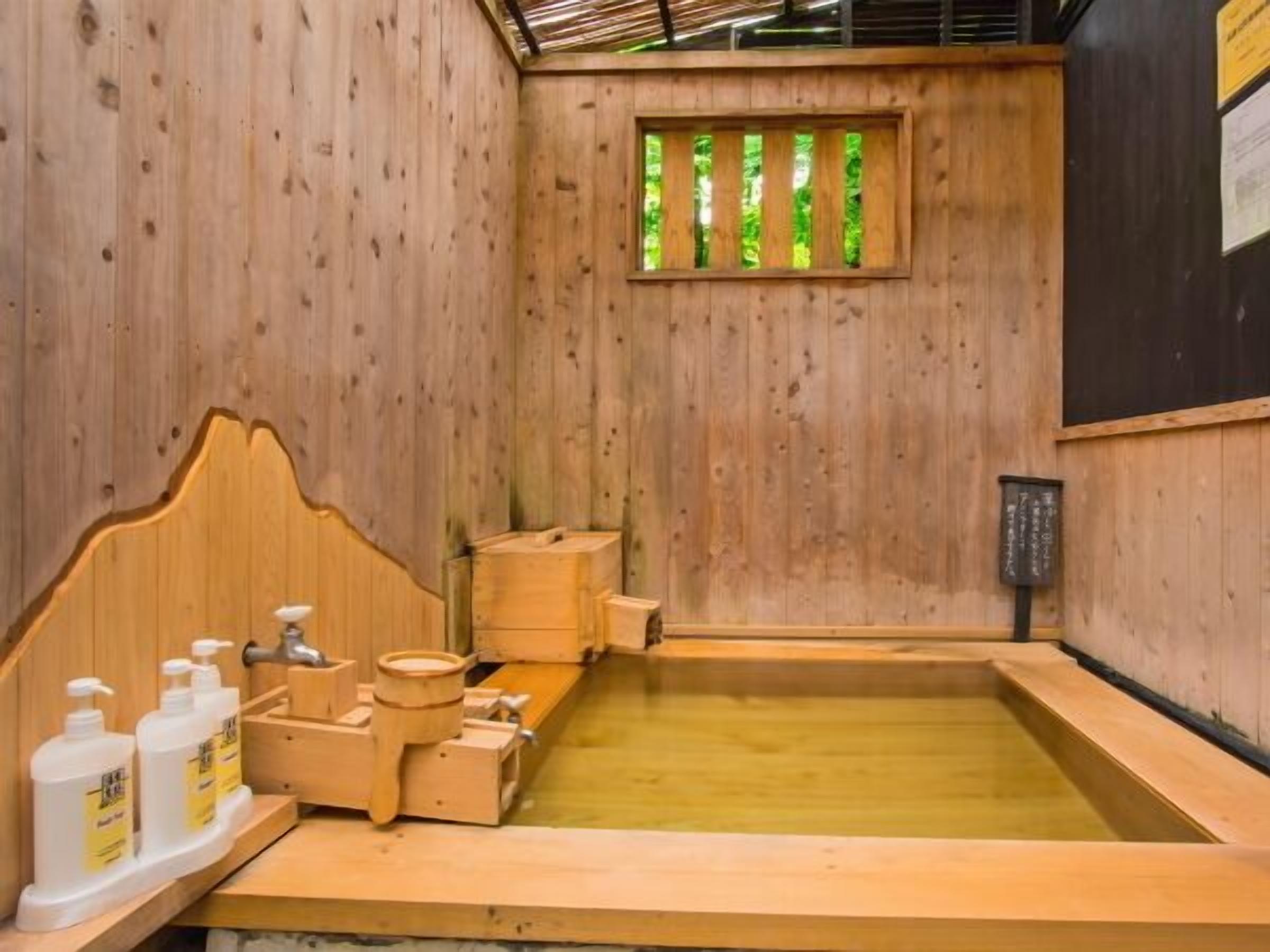 Una habitación de madera con una bañera de madera, bancos de madera y una ventana con listones verticales.