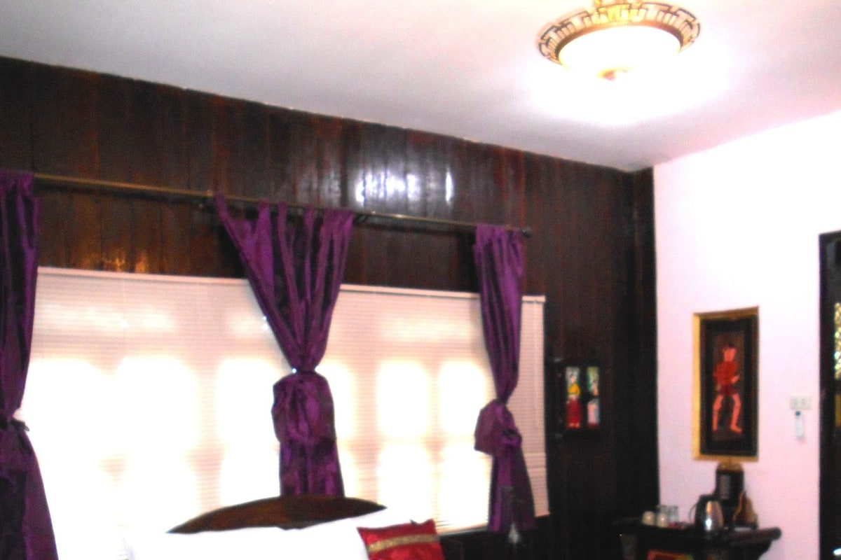 Ein Schlafzimmer mit einem großen Bett, violetten Vorhängen, einer Kristallleuchtre und einem Nachttisch mit Lampe.
