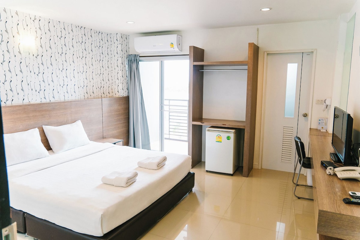 A hotel room with a bed, a desk with a computer, a mini-fridge, and a TV.