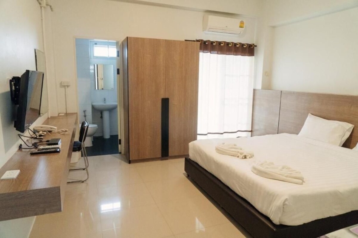 A hotel room with a bed, a desk with a telephone, a mirror, a bathroom with a sink, and a window with curtains.