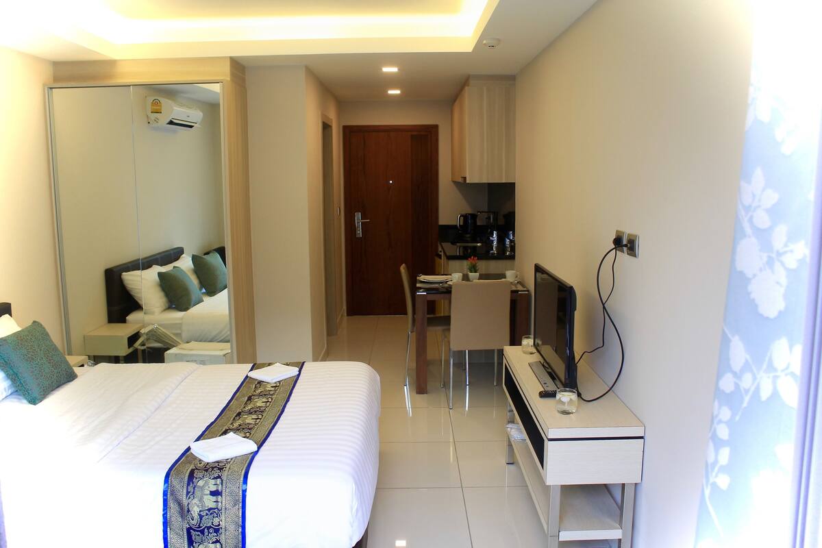 Ein Hotelzimmer mit Bett, Schreibtisch mit Fernseher, Spiegel und einer Küchenzeile.