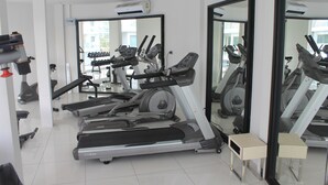 Une salle de sport équipée de tapis de course, de vélos d’appartement et d’un banc de musculation.