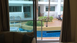 Une chambre avec vue sur une piscine, un balcon avec des chaises et un canapé avec des coussins.