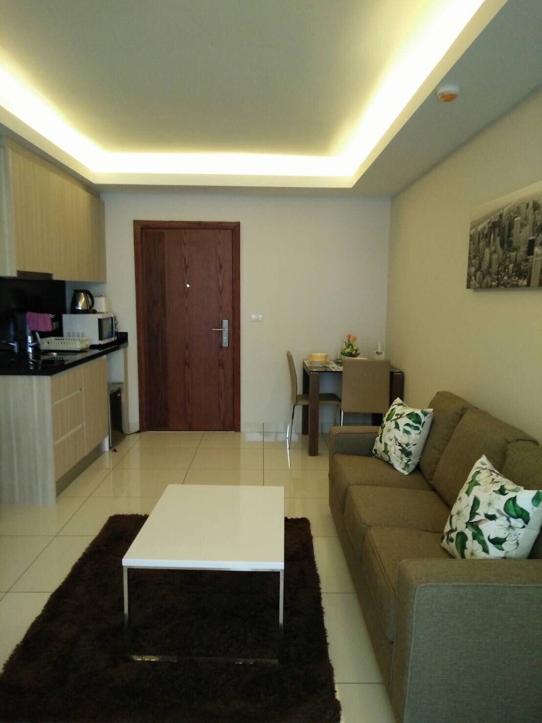 A modern living room with a white coffee table, a brown sofa with floral cushions, and a dining area with a small table and chairs.
