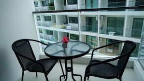 Un balcon doté d’une table en verre et de deux chaises, offrant une vue sur un immeuble comportant de nombreux balcons et des unités de climatisation.