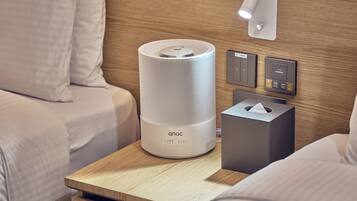A modern hotel room with a bedside table featuring a white bedside lamp, a tissue box, and a control panel for the lamp.