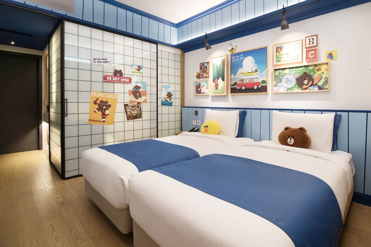 Ein Hotelzimmer mit zwei Betten, einem Kleiderschrank und einer Wand, die mit Kinderzeichnungen verziert ist.