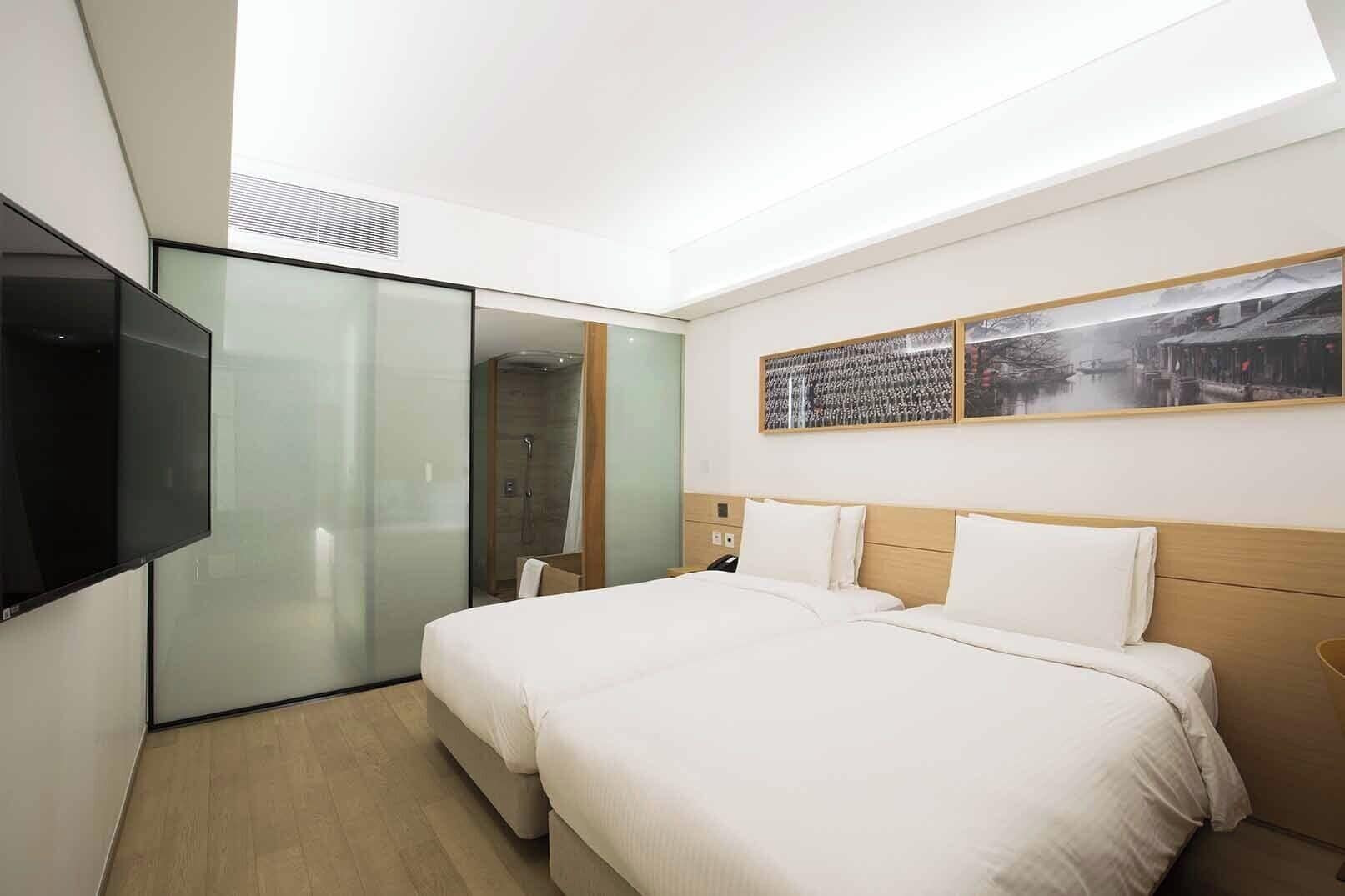 Una habitación de hotel moderna con una cama grande, un televisor montado en la pared y un armario con puerta corredera de vidrio.