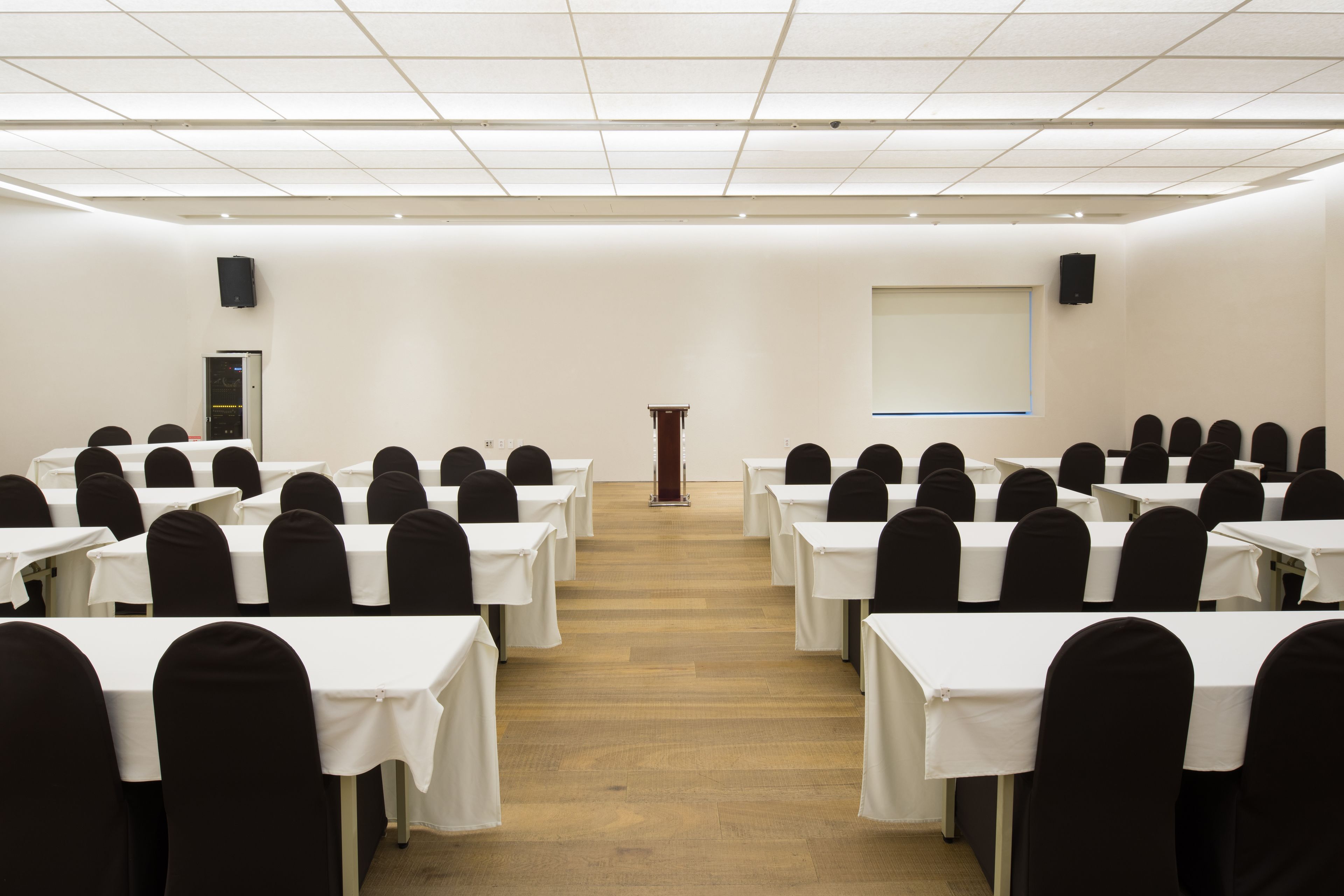 Un salón de conferencias con filas de mesas y sillas, un atril y una pantalla de proyección.
