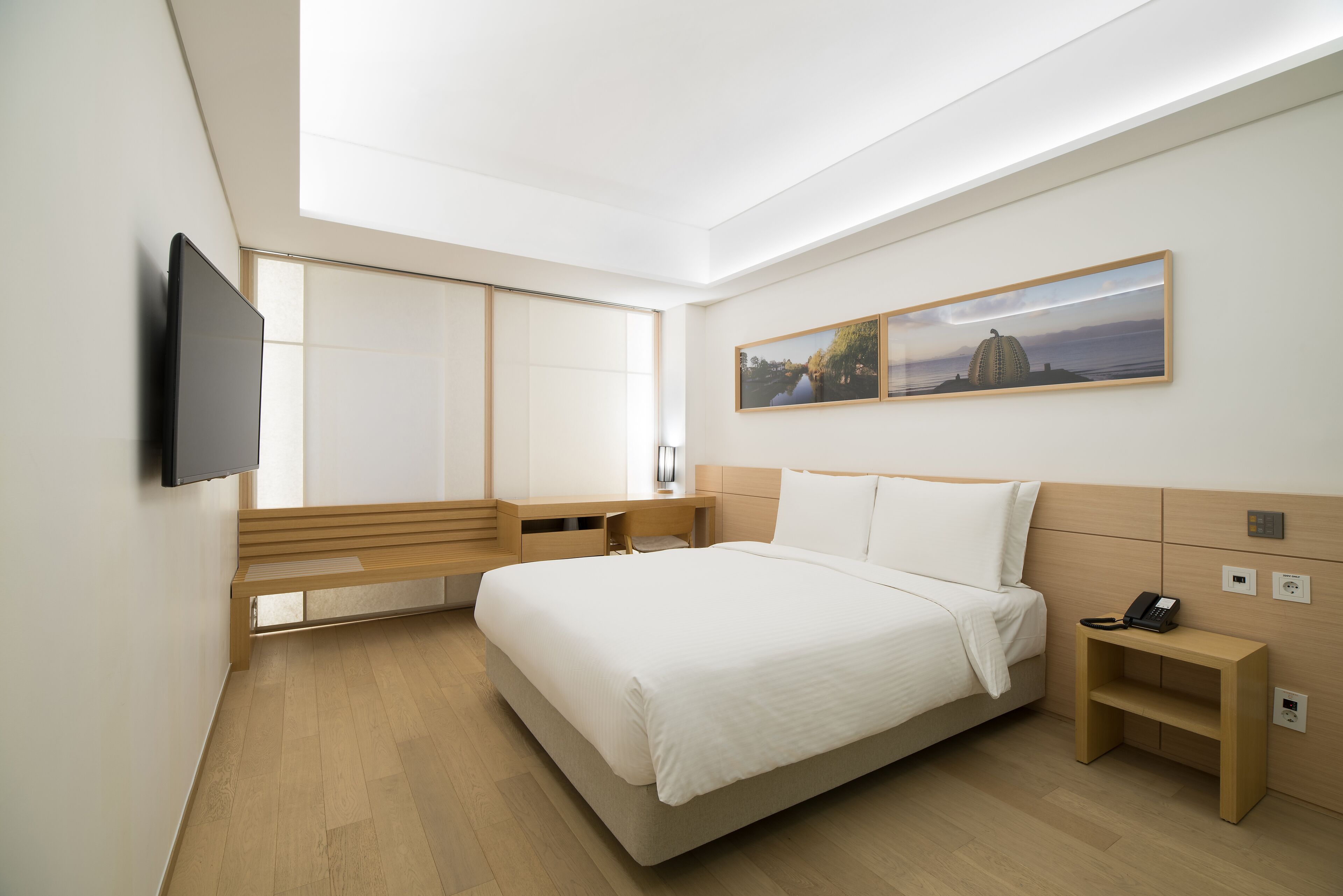 Une chambre d’hôtel moderne dotée d’un grand lit, d’une table de chevet avec un téléphone, d’un téléviseur fixé au mur et d’une grande fenêtre offrant une vue sur la ville.