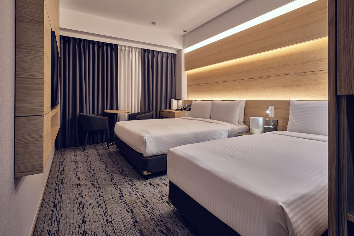 Ein modernes Hotelzimmer mit zwei Betten, einem kleinen Tisch, einem Stuhl und einem Schreibtisch mit einer Lampe.