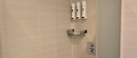 A modern shower with a glass door, a handheld showerhead, and toiletries on the wall.