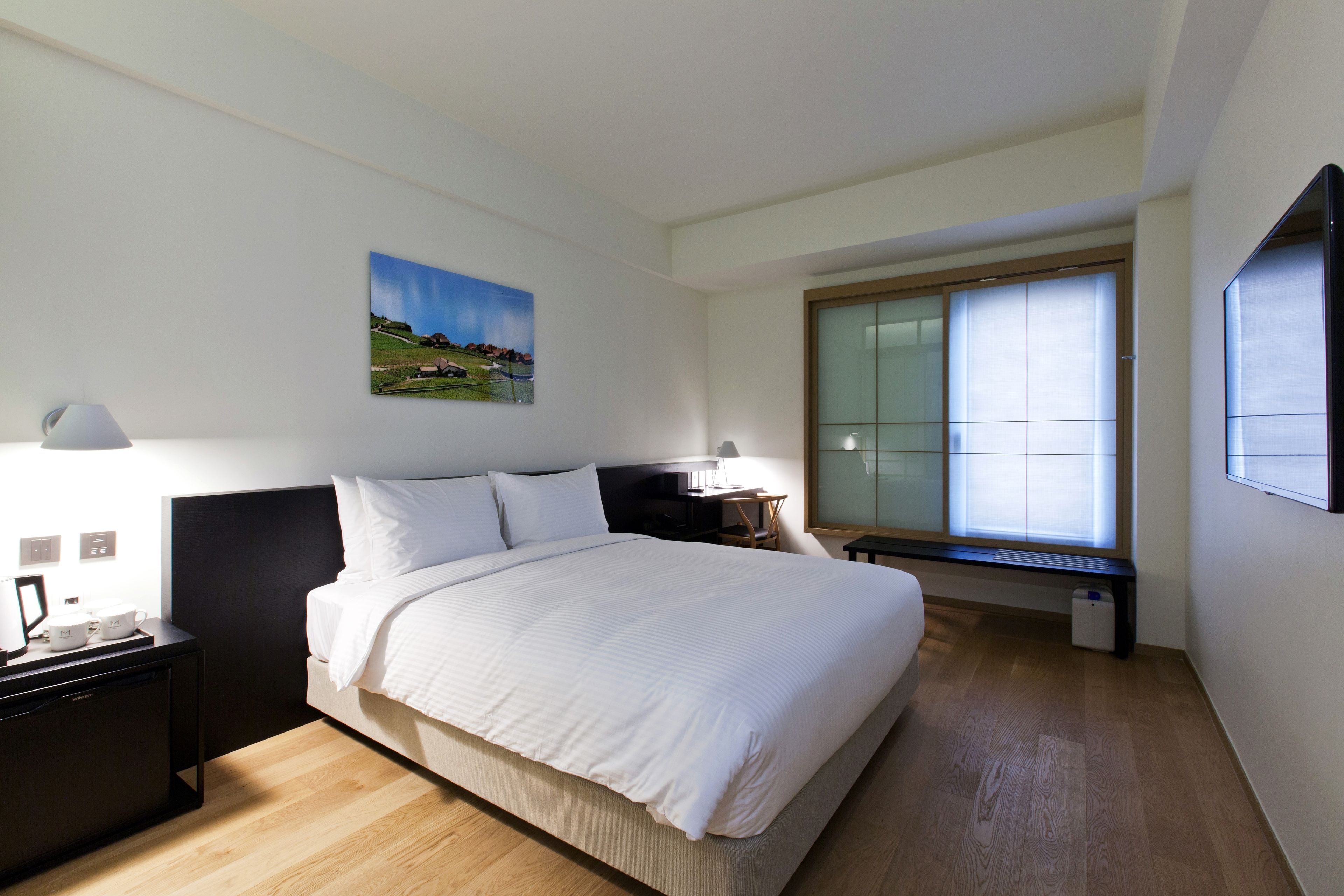 Een moderne hotelkamer met een groot bed, nachtkastjes, een bureau en een raam met jaloezieën.