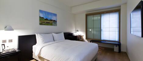 Een moderne hotelkamer met een groot bed, nachtkastjes, een bureau en een raam met jaloezieën.
