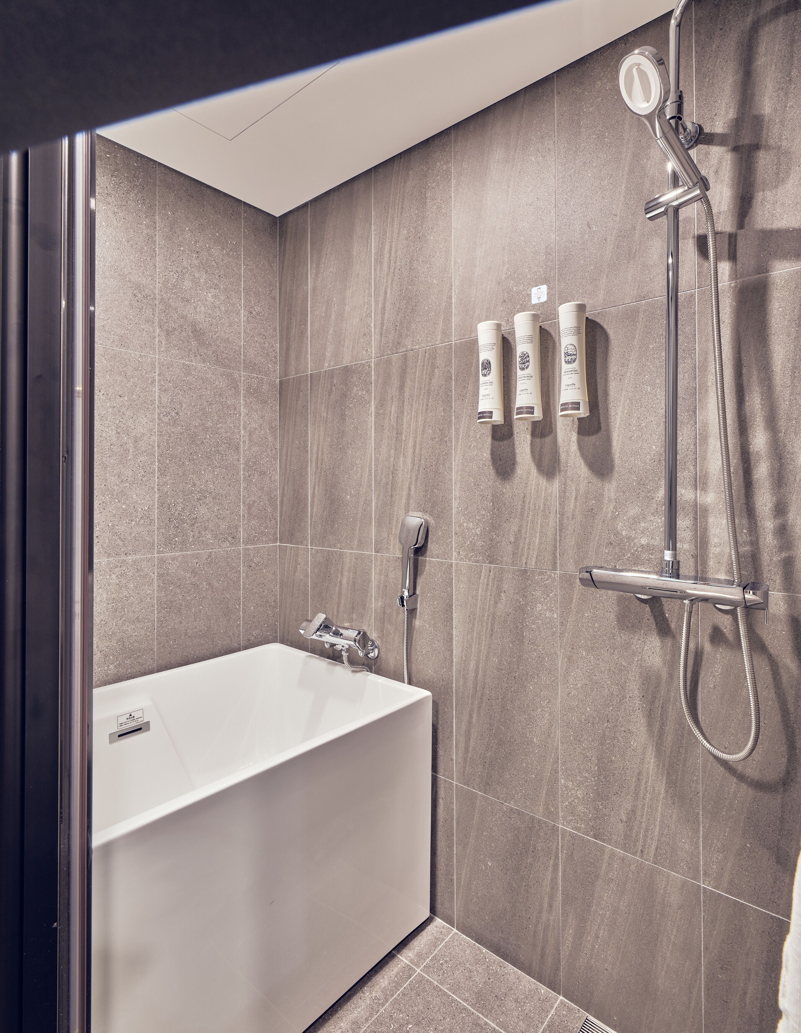 Une salle de bain moderne avec une baignoire, une douchette à main et deux bouteilles de shampoing.