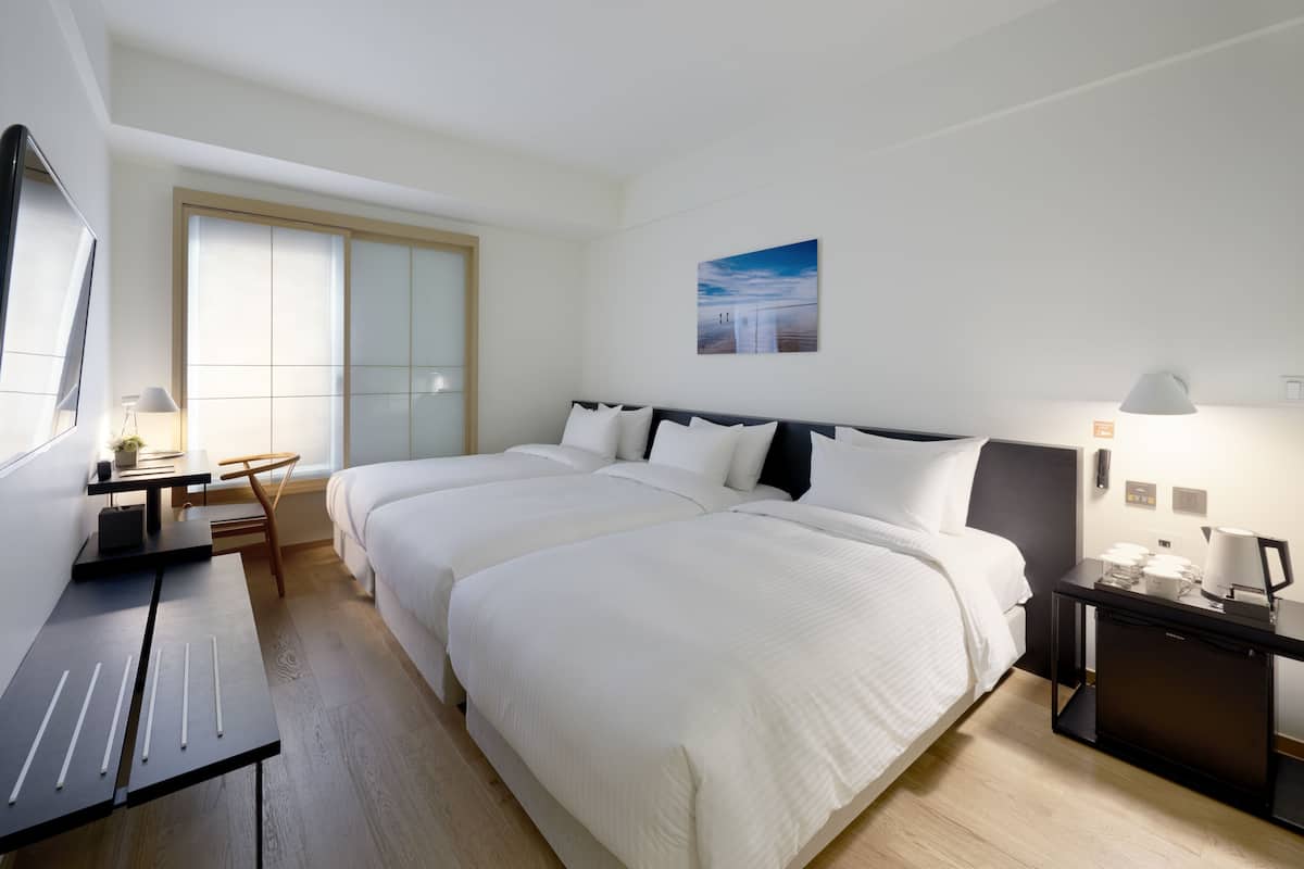 Ein Hotelzimmer mit zwei Betten, einem Schreibtisch, einem Sessel, einem Fernseher und einem Bild an der Wand.