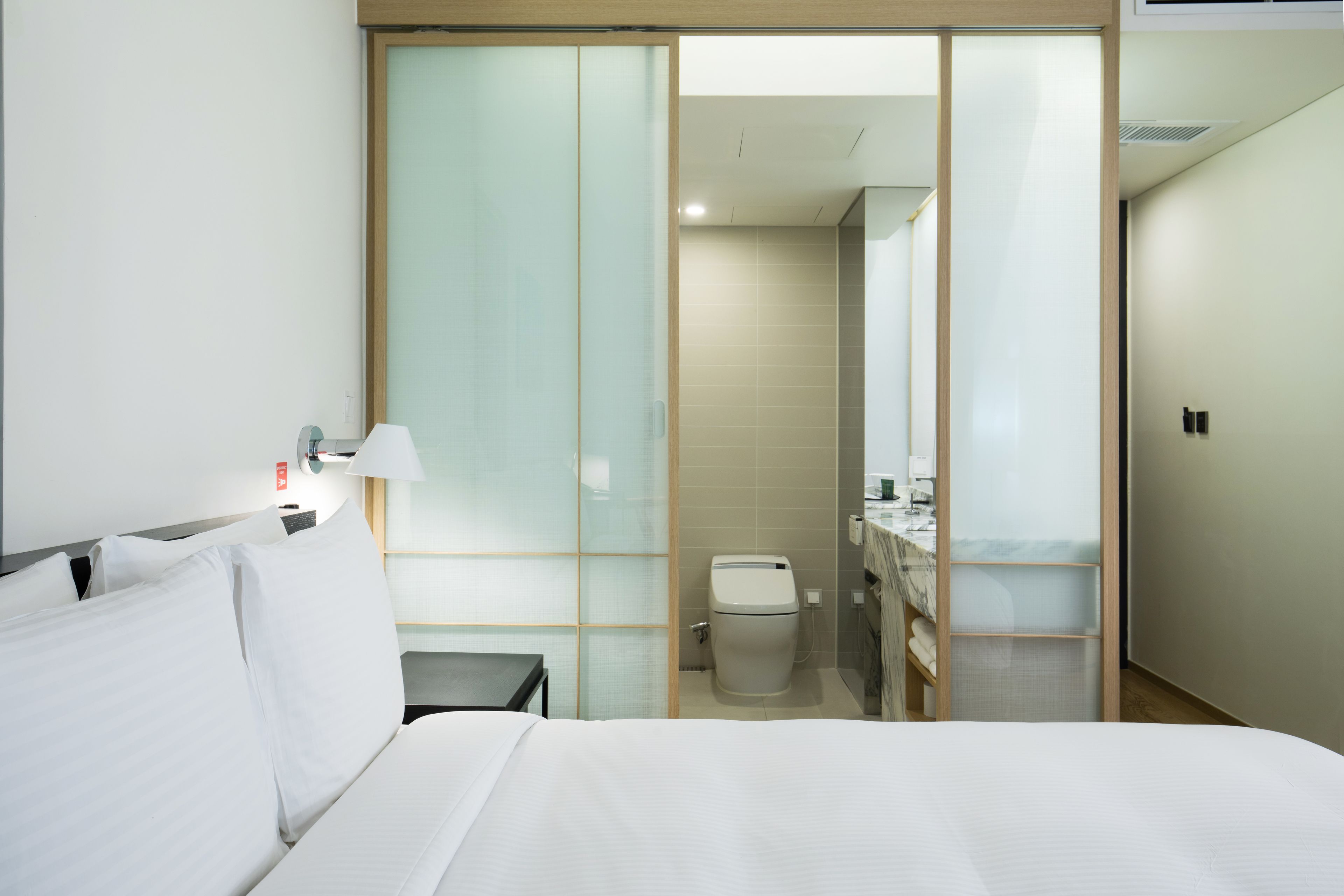 Une chambre d’hôtel comprenant un lit, une table de chevet, une lampe, des toilettes et un espace douche.