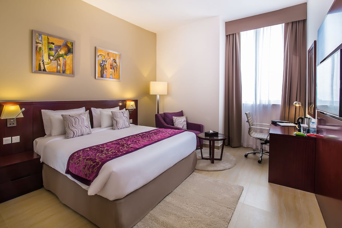 A hotel room with a large bed, a desk, a chair, and two paintings on the wall.