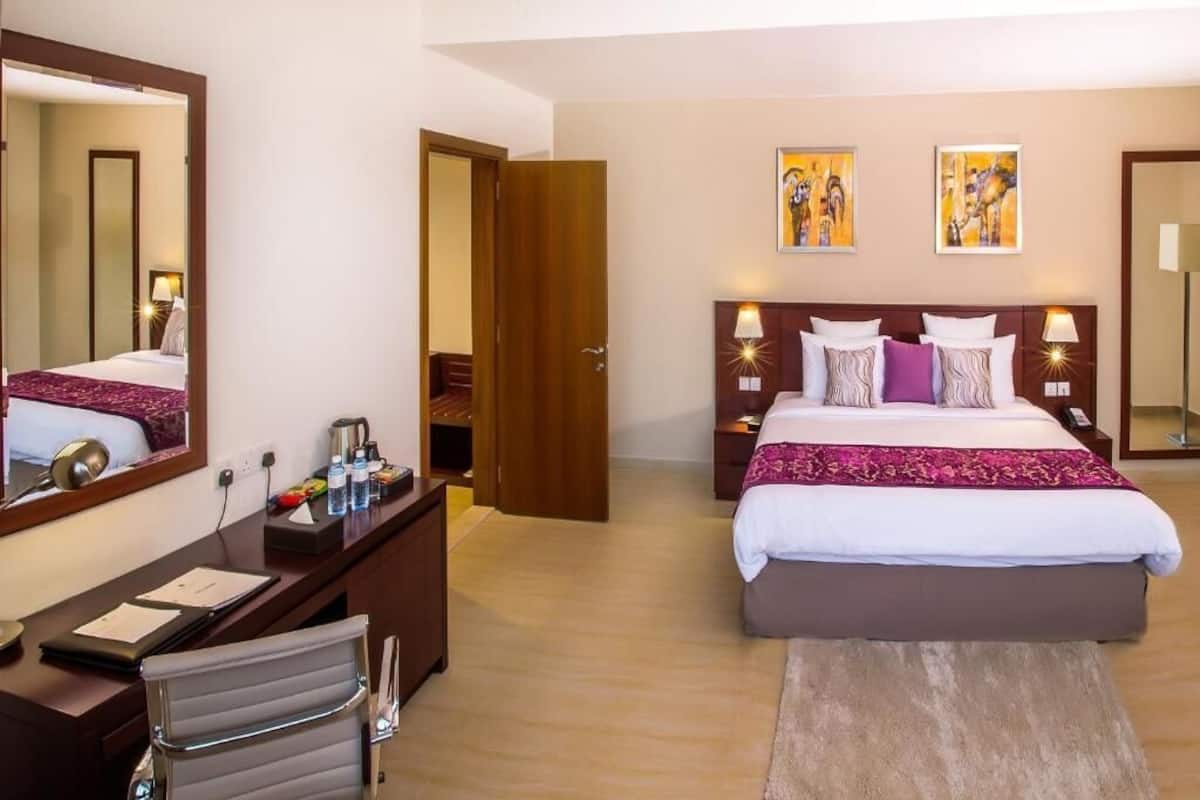 A hotel room with a large bed, a desk with a chair, a mirror, and two paintings on the wall.