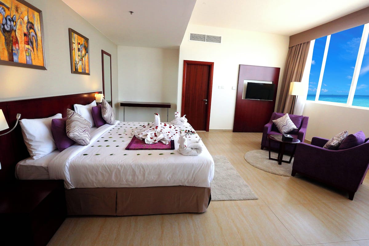 A hotel room with a large bed, a seating area with a purple sofa, a television, and a view of the ocean.