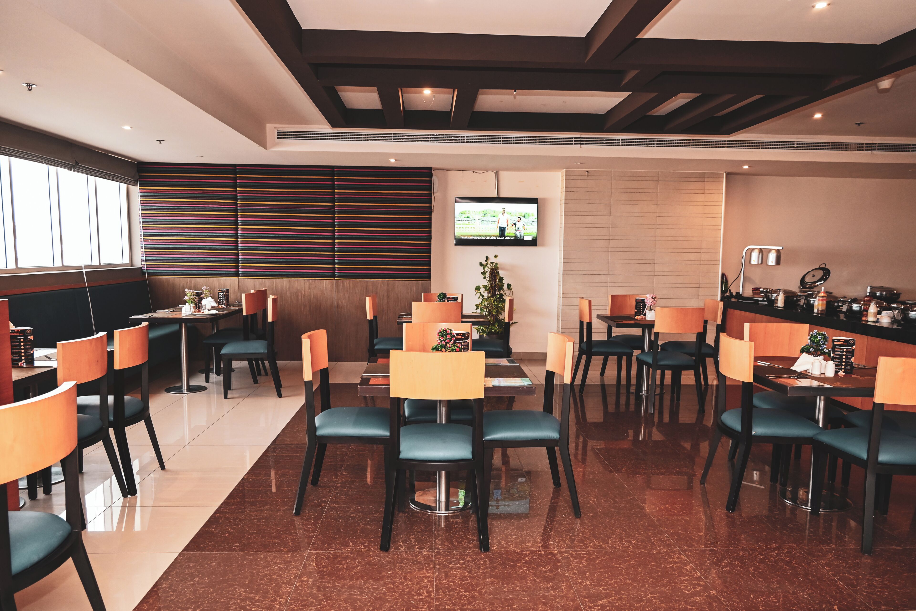 Um restaurante moderno com várias mesas e cadeiras, uma televisão presa na parede e um design de parede com ripas de madeira.