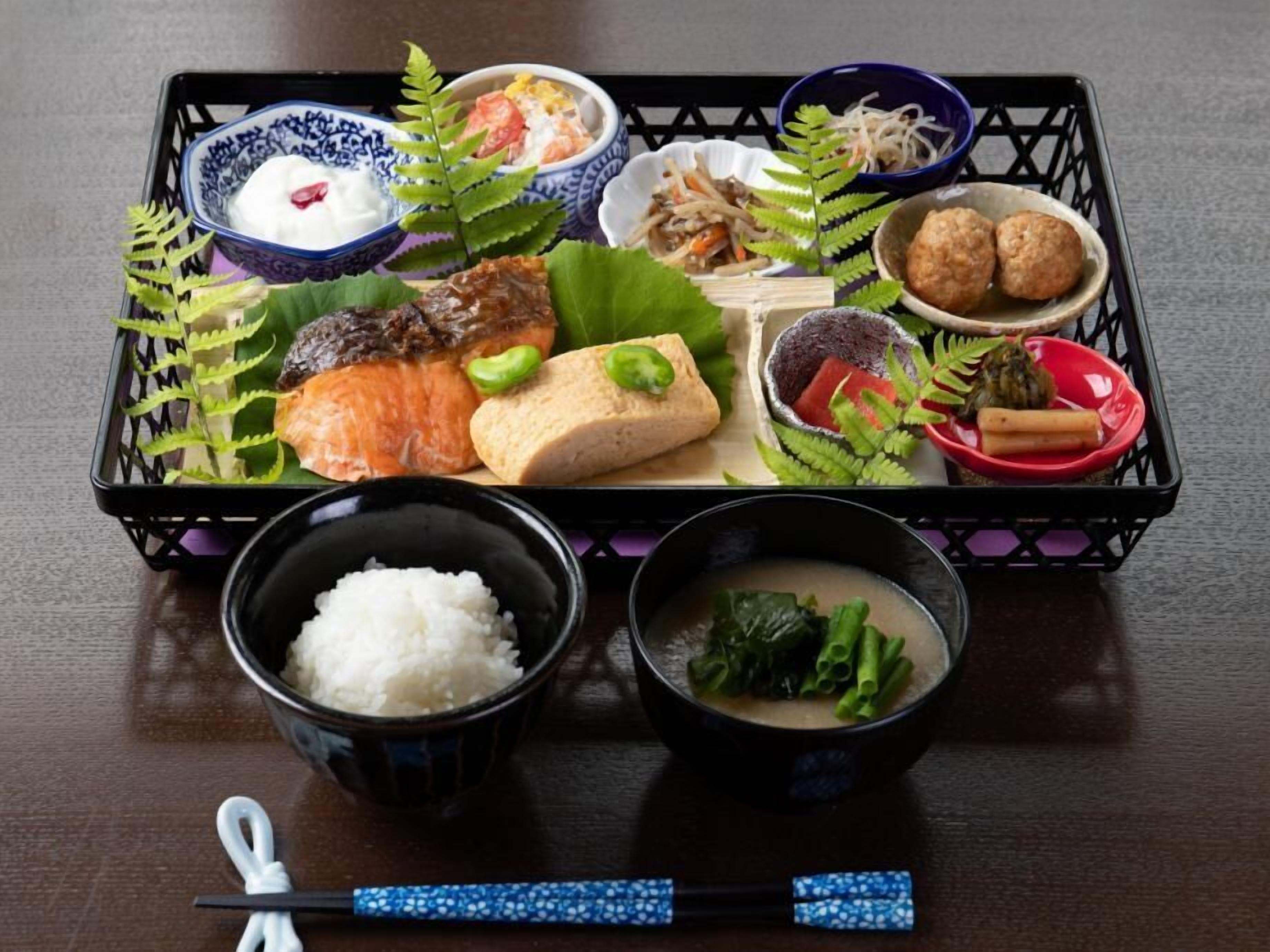 A traditional Japanese meal set on a black tray with various dishes including rice, soup, and meat.