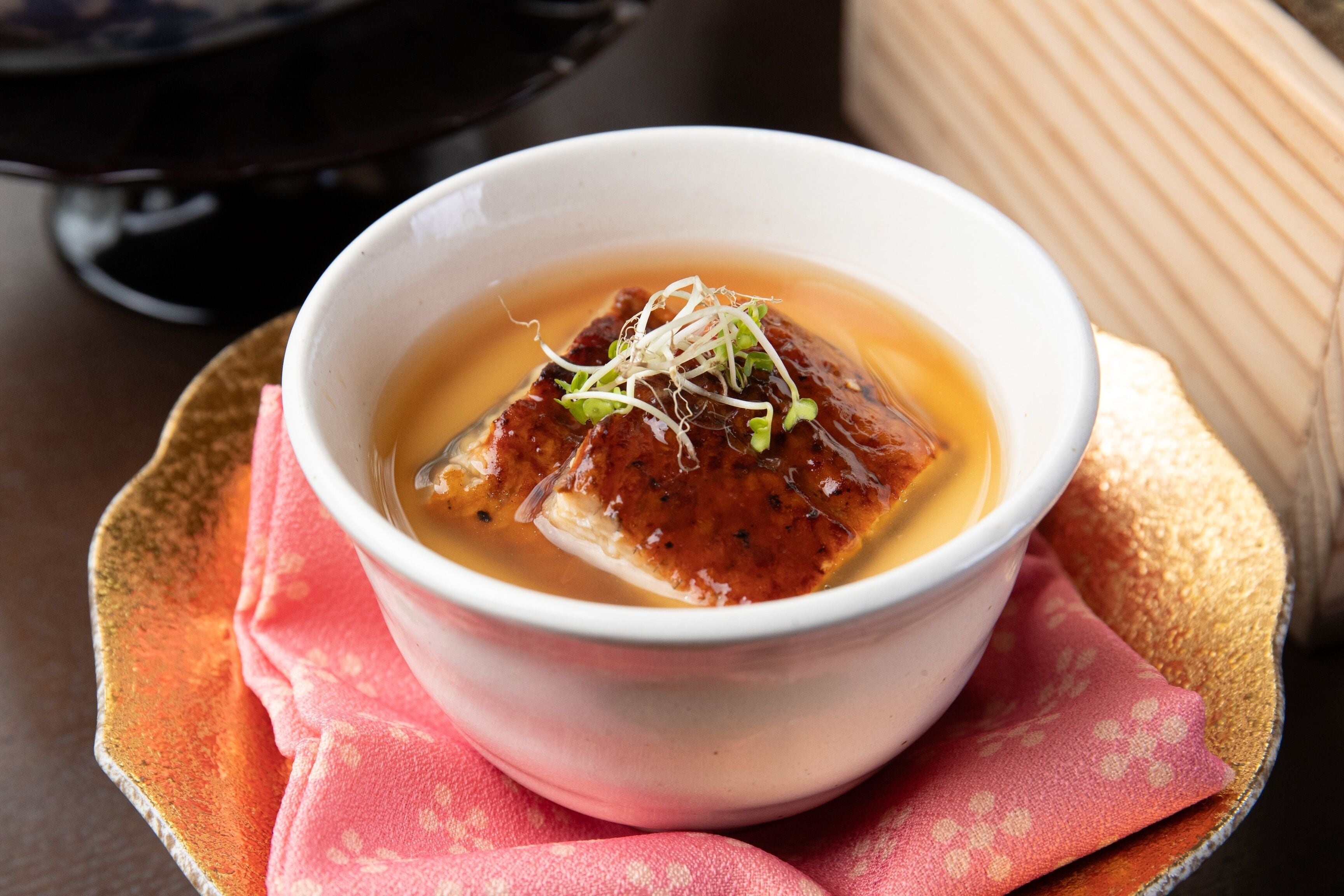 A bowl of soup with a piece of tofu and sprouts on a pink napkin.