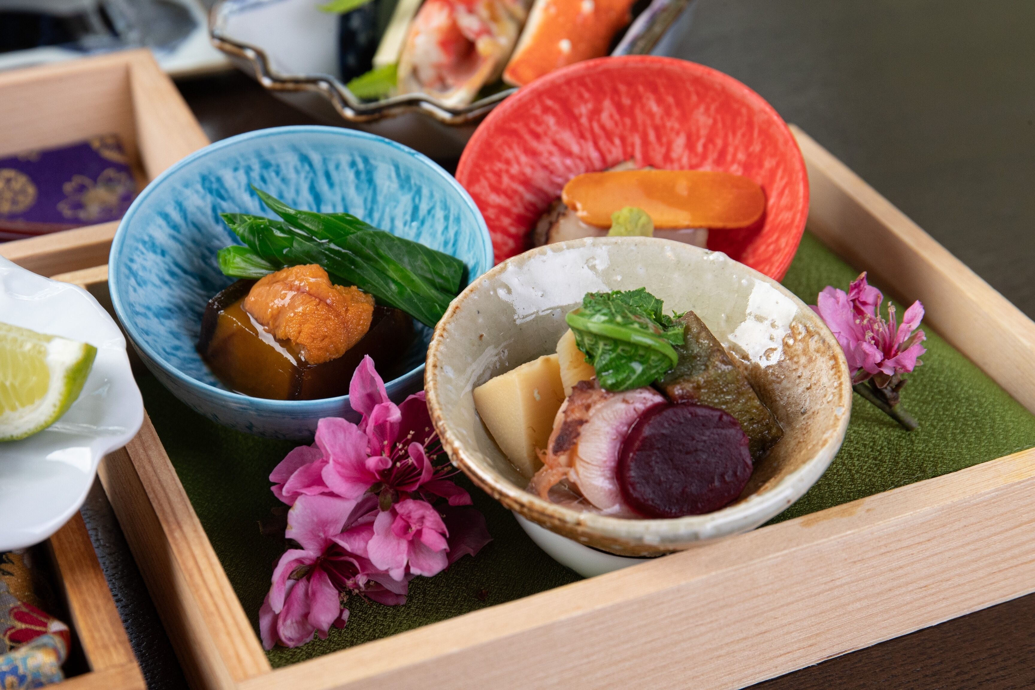 A tray with various dishes, including a bowl with a green vegetable and a bowl with a red vegetable, both on a green mat.