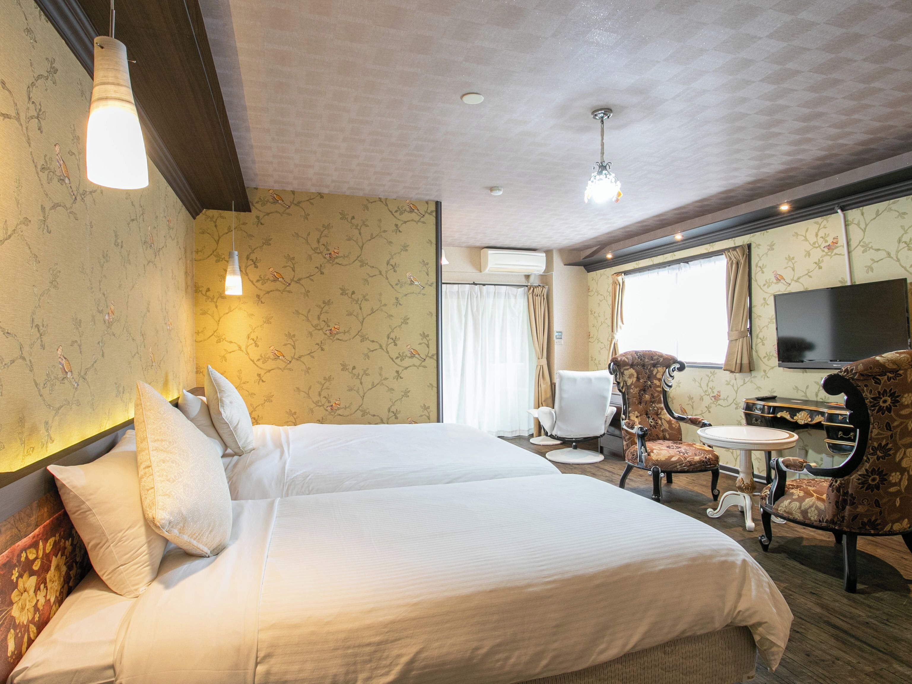 A hotel room with a large bed, two armchairs, a small table, a TV, and a window with curtains.