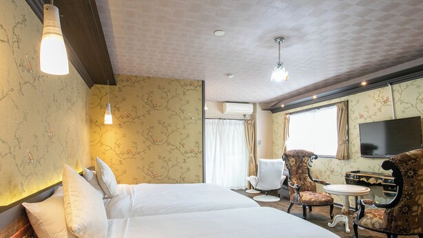 A hotel room with a large bed, two armchairs, a small table, a TV, and a window with curtains. - Yufuin Besso Shikisai Hotel (Yufu)