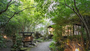 A pathway leading to a traditional building surrounded by lush greenery and rocks. - Yufuin Besso Shikisai Hotel (Yufu)