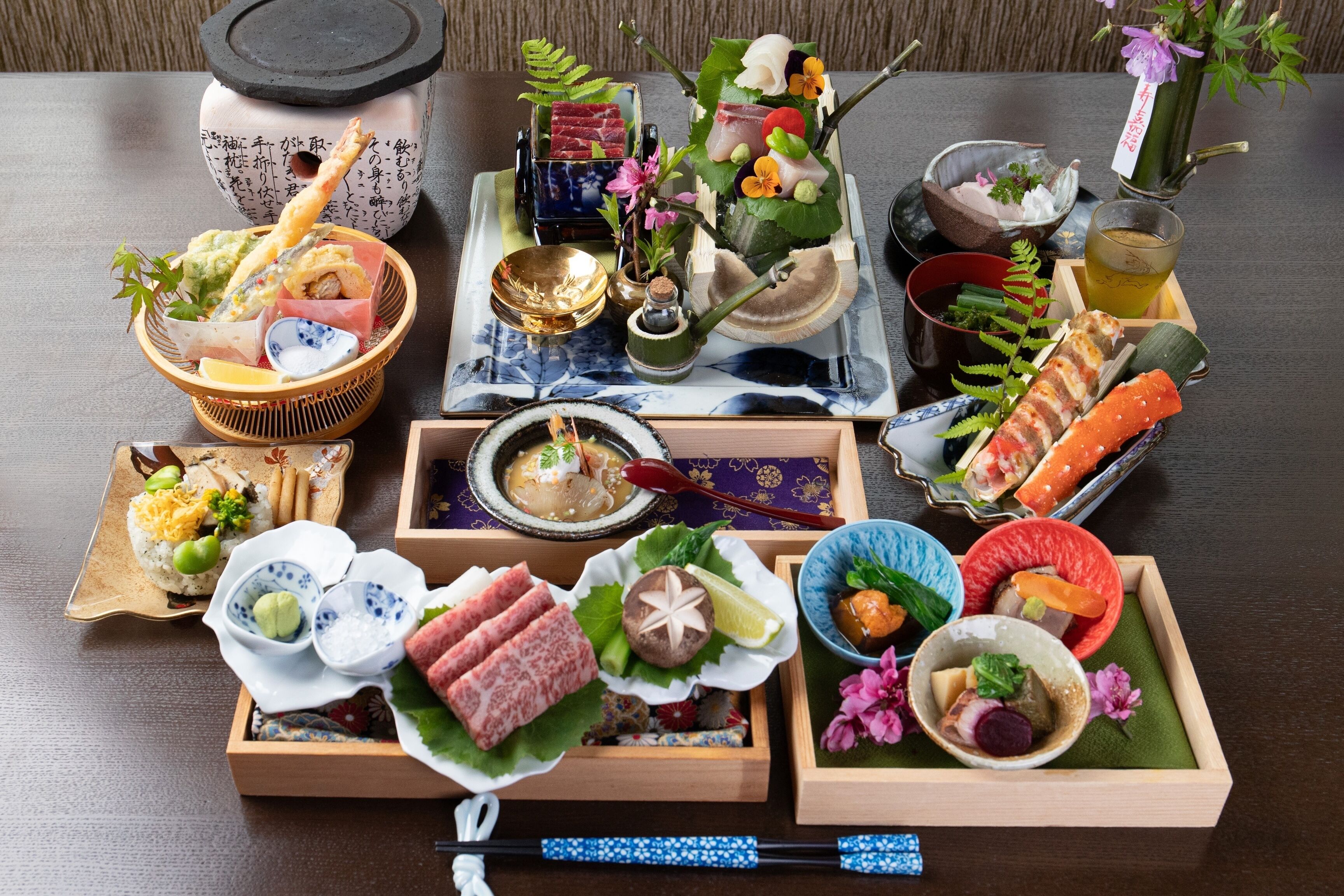 Variedad de platos japoneses sobre una mesa, incluyendo sushi, sashimi y otras exquisiteces, con palillos y cuencos pequeños.