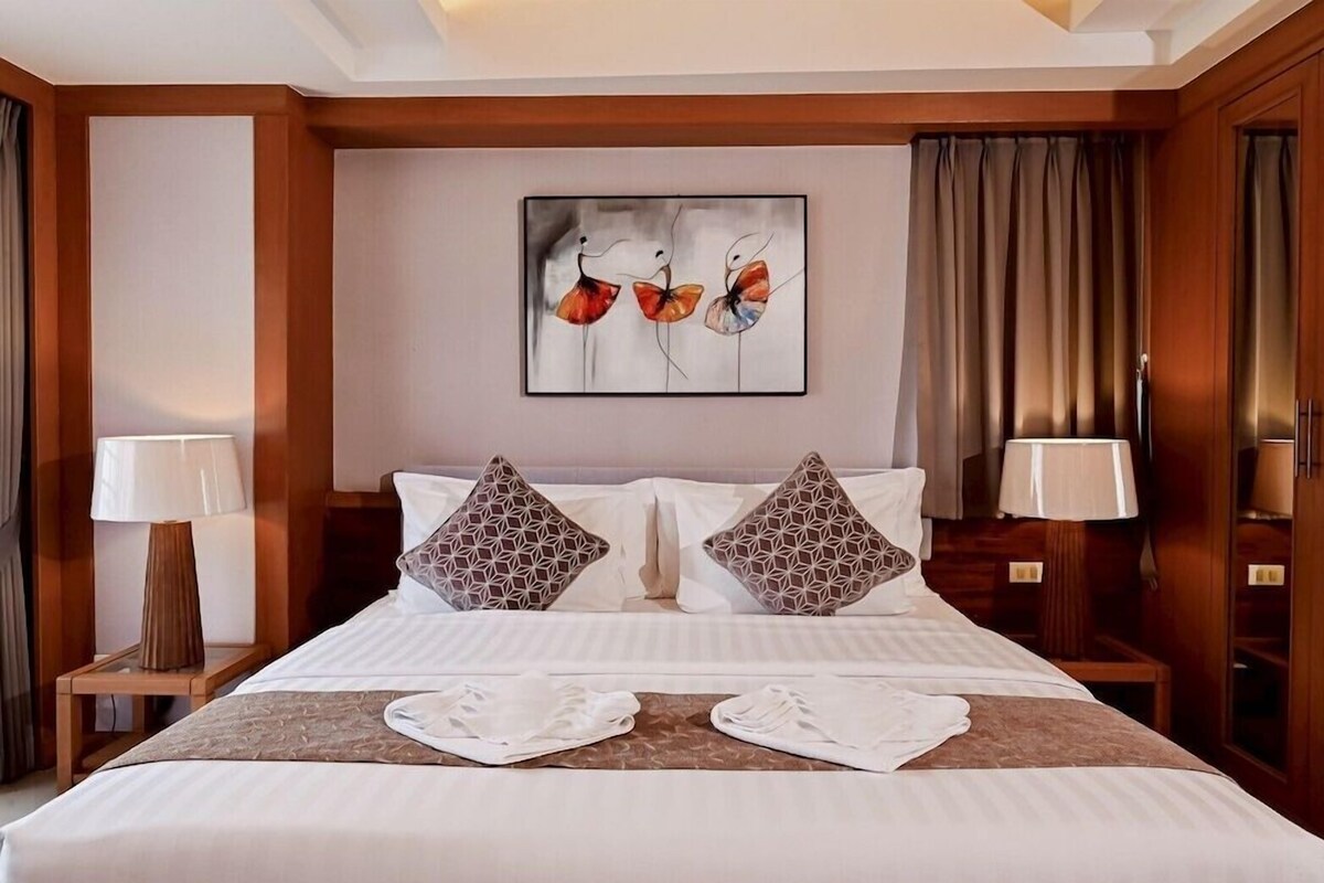 A hotel room with a bed, two nightstands, a painting, and a window with curtains.