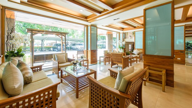 Un vestíbulo amplio con mobiliario de madera, una mesa de centro de vidrio y grandes ventanales con vistas al exterior.