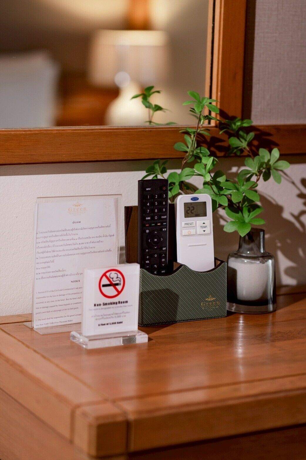 A wooden table with a digital thermostat, a black telephone, a green plant, and a "No Smoking" sign.