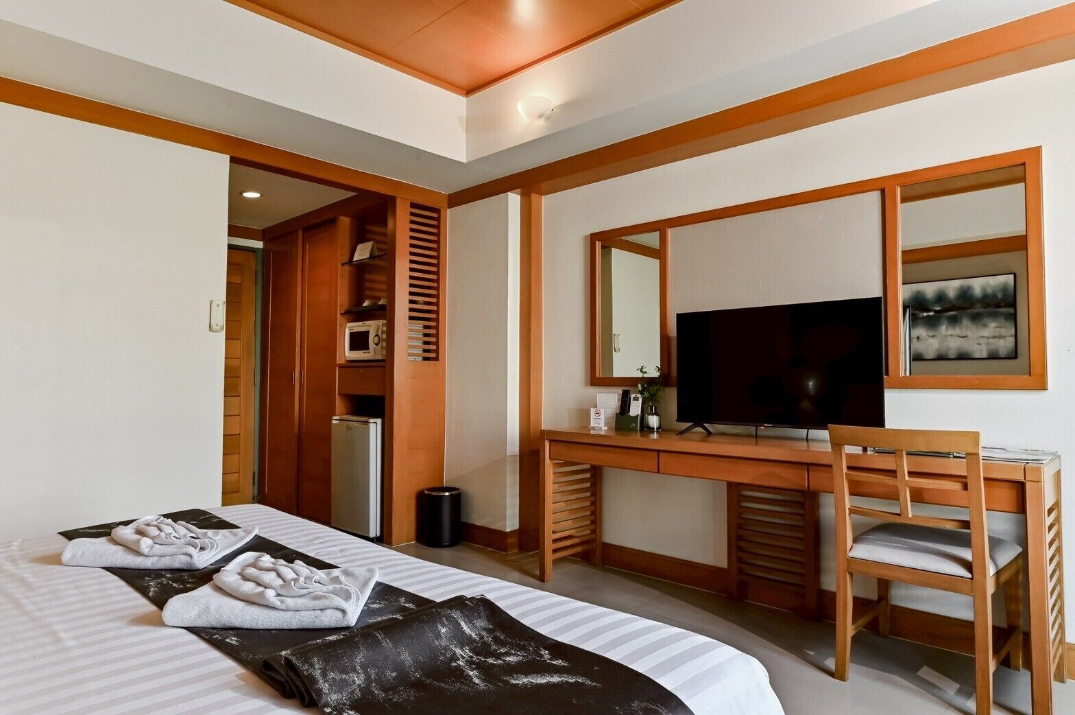 A hotel room with a bed, a desk with a TV, a mirror, and a small kitchenette.