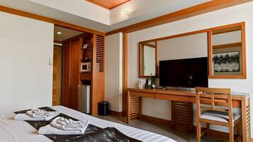 A hotel room with a bed, a desk with a TV, a mirror, and a small kitchenette.
