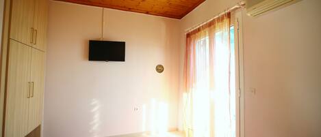A room with a wooden ceiling, a flat-screen TV mounted on the wall, and a bed with a pink cover.