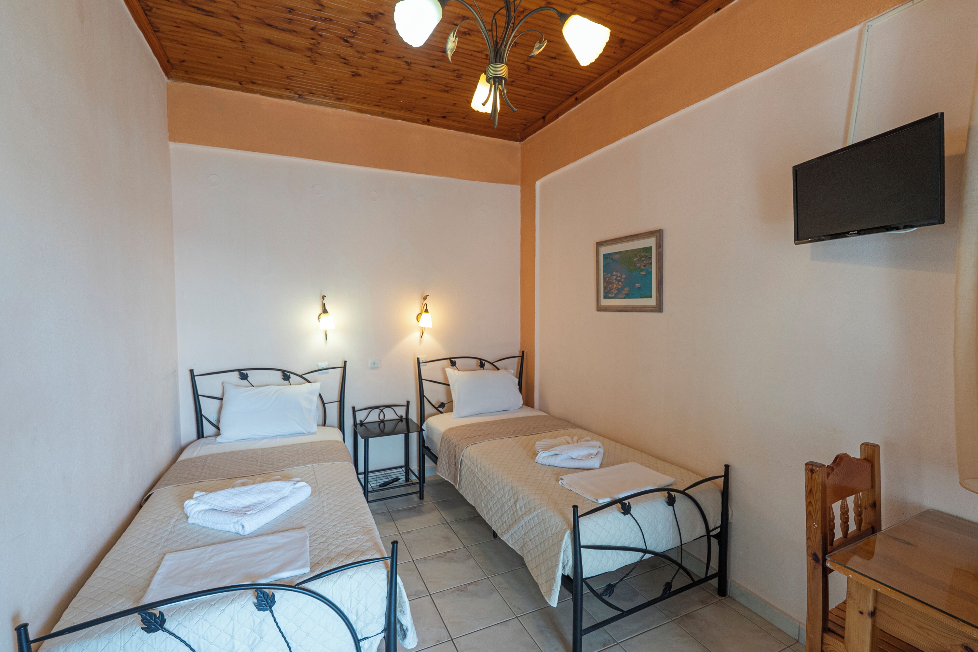 Una habitación con dos camas individuales, una mesita pequeña, una silla, un televisor montado en la pared y una lámpara en el techo.