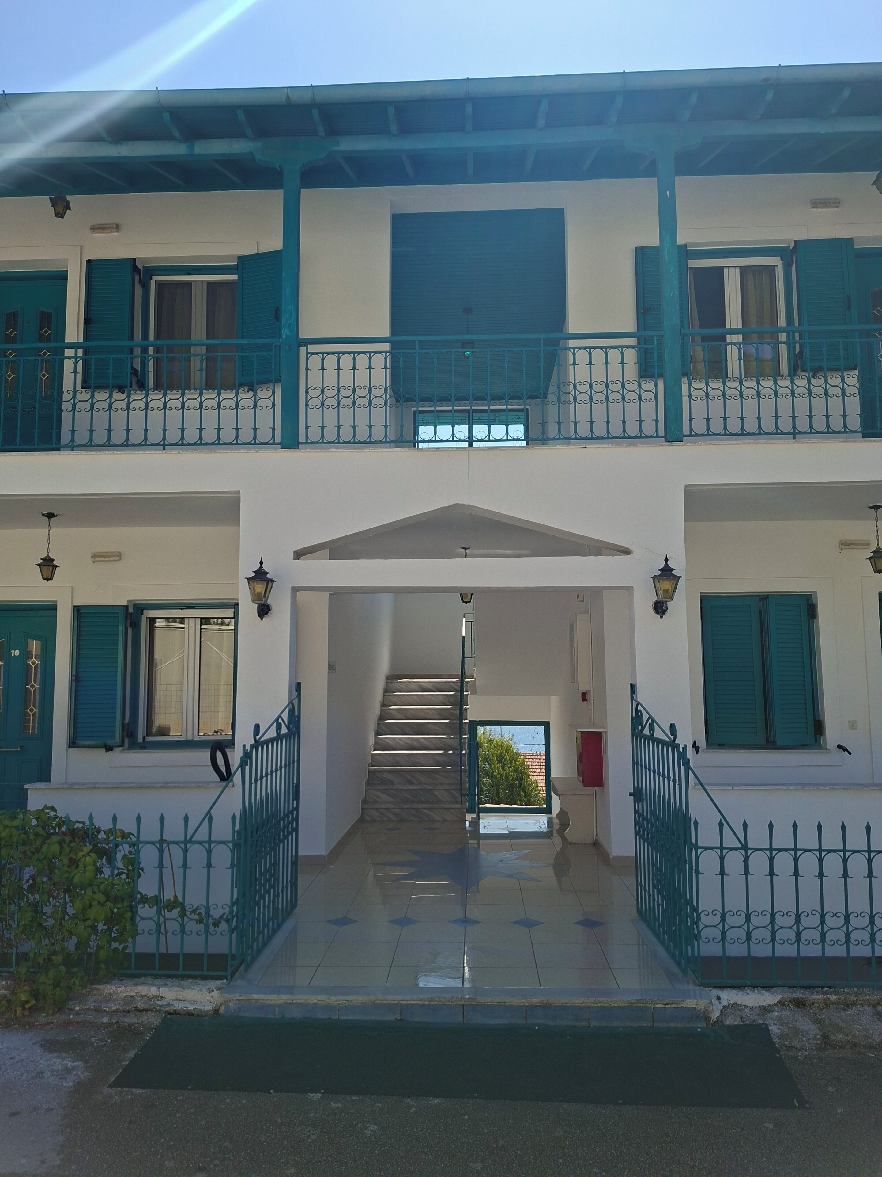 A two-story building with a central staircase, green shutters, and a gated entrance.