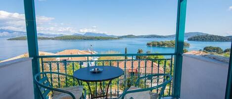 A balcony with a table and chairs, overlooking a lake and distant islands.